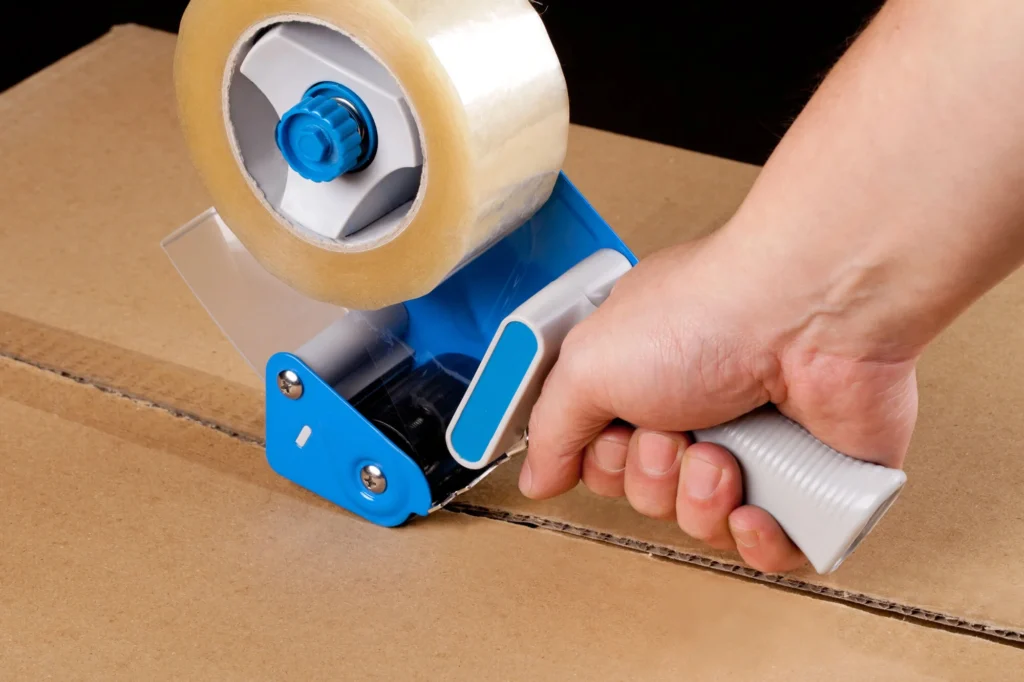 Close-up of hands sealing a cardboard box with packing tape – Movers In Katy, TX
