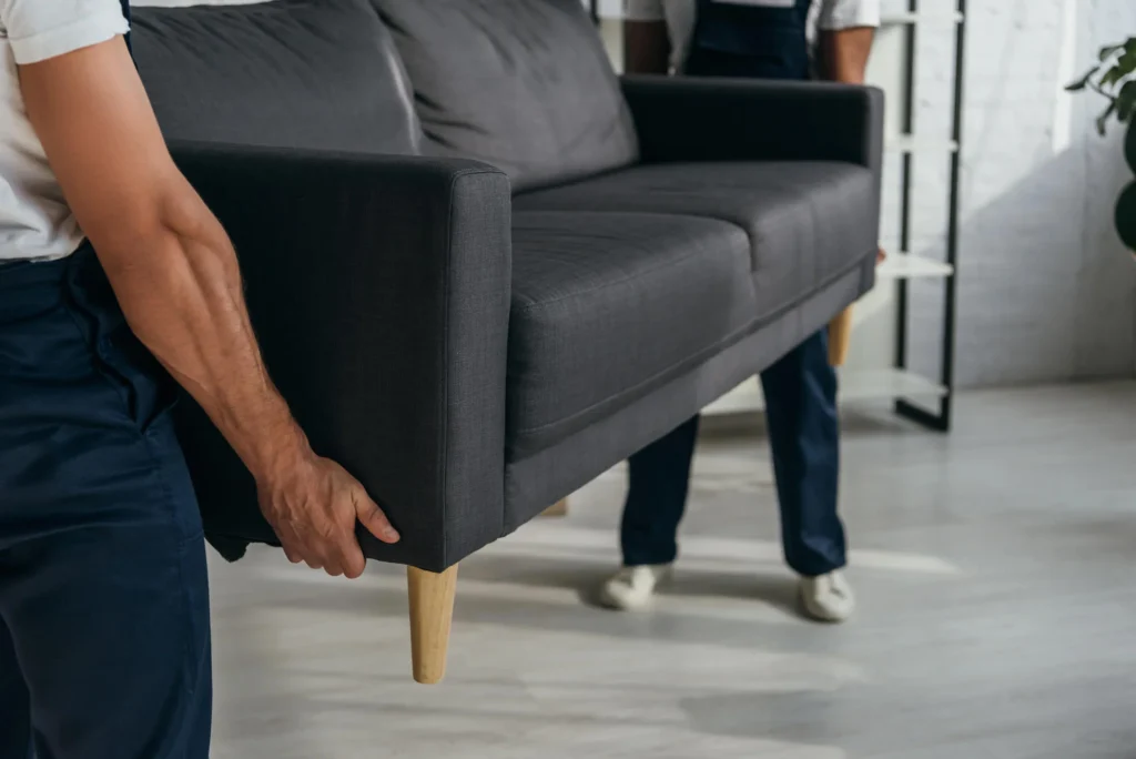 Professional movers lifting a dark gray sofa together inside a modern home – Movers in Kansas City, MO