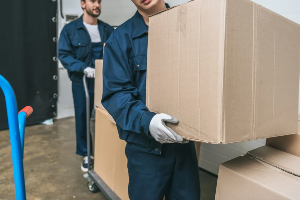 Two movers in blue uniforms carrying a large cardboard box inside a building – Movers in Florence, KY