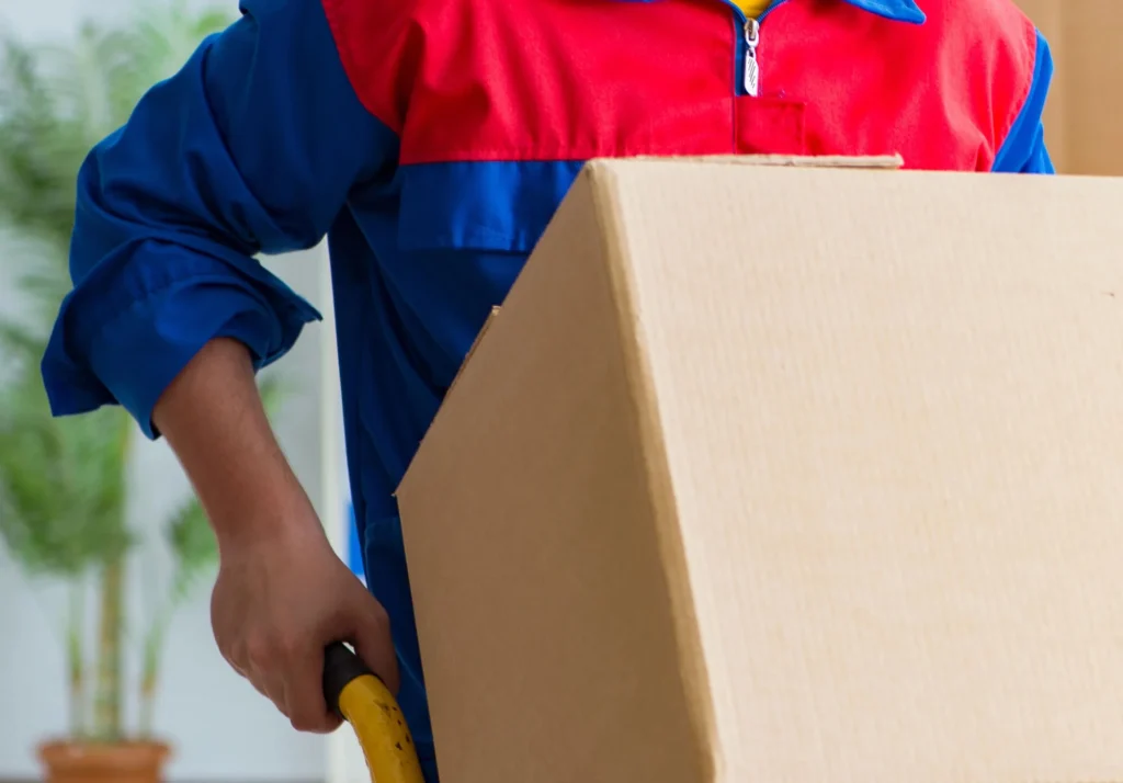 Worker in red and blue uniform handling a cardboard box with a dolly – Movers In Katy, TX
