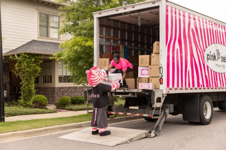 Two movers unloading a Pink Zebra Moving truck